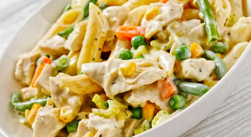 Penne z kurczakiem i warzywami w kremowym sosie. Danie zawiera zieloną fasolkę, groszek, kukurydzę i marchewkę.