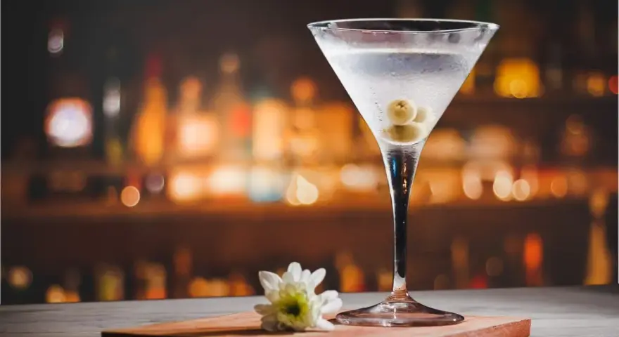 Kieliszek martini z oliwkami i kwiatkiem na blacie. Idealny dodatek do drinka, by wiedzieć, z czym pić martini.