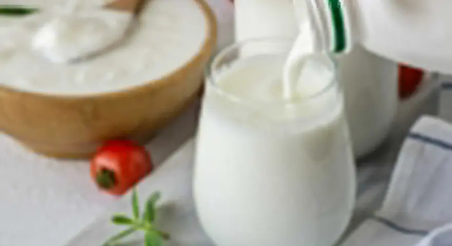 Ayran co to? Orzeźwiający napój mleczny, idealny na upalne dni, nalewany do szklanki. Obok miska z jogurtem i pomidorek.